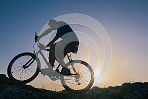 Silhouette of a fit male mountain biker riding his bike uphill on rocky harsh terrain on a sunset