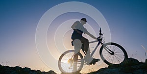 Silhouette of a fit male mountain biker riding his bike uphill on rocky harsh terrain on a sunset