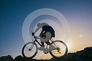 Silhouette of a fit male mountain biker riding his bike uphill on rocky harsh terrain on a sunset