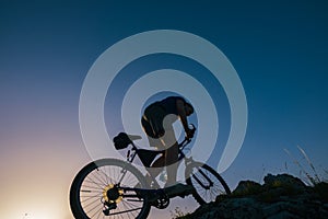 Silhouette of a fit male mountain biker riding his bike uphill on rocky harsh terrain on a sunset