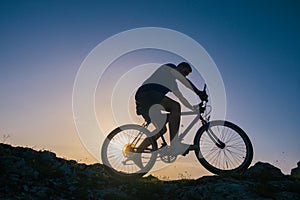 Silhouette of a fit male mountain biker riding his bike uphill on rocky harsh terrain on a sunset