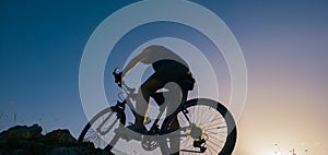 Silhouette of a fit male mountain biker riding his bike uphill on rocky harsh terrain on a sunset