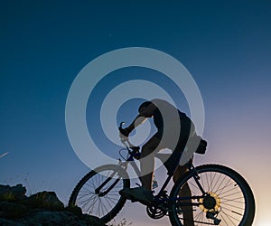 Silhouette of a fit male mountain biker riding his bike uphill on rocky harsh terrain on a sunset