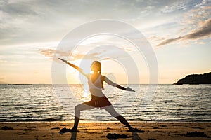 Silhouette of a fit woman practicing the warrior yoga pose at sunset