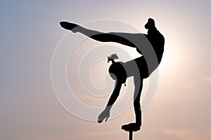 Silhouette of flexible acrobat doing handstand on the dramatic sunset background. Concept of individuality, creativity
