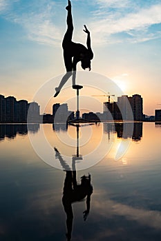 Silhouette of flexible acrobat doing handstand on the dramatic sunset and cityscape background. Concept of individuality