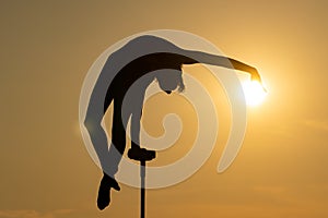 Silhouette of flexible acrobat doing handstand and touching the sun disc on the dramatic sunset background. Concept of