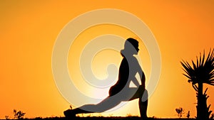 Silhouette of flexible female practicing yoga on mountain top at sunset, sport