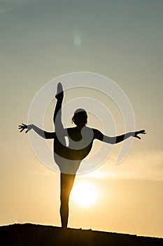 Silhouette of flexible and fit girl keeping balance in split on sunset background. Concept of yoga, meditation and