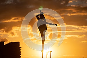 Silhouette of flexible and fit girl standing on fit with split and keeping balance against dramatic sunset Concept of