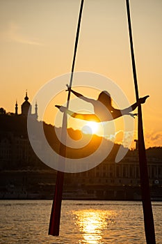 Silhouette of a flexible woman acrobat on aerial silk during a sunset on Kiev city background. concept of freedom and