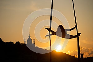 Silhouette of a flexible woman acrobat on aerial silk during a sunset on Kiev city background. concept of freedom and