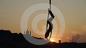 Silhouette of a flexible woman acrobat on aerial silk during a sunset on Kiev city background. concept of freedom and