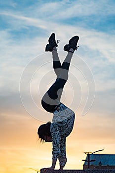 Silhouette of flexible woman gymnast doing handstand on the dramatic sunset. Concept of willpower, motivation and