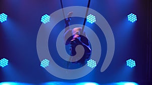 Silhouette of flexible woman hanging in an aerial acrobatics ring performs complex tricks. Aerial acrobat close up in a