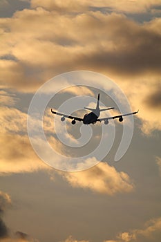 Silhouette of a flying airplane against a sunset sky with golden clouds - suitable for a wallpaper