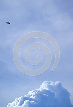 Silhouette of a flying airplane on bright blue cloudy sky with cumulus clouds at below