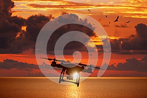 Silhouette of flying drone in glowing red sunset sky above sea