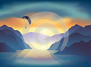 Silhouette of flying paraglider, who take a selfie with action camera above the mountain lake at sunrise