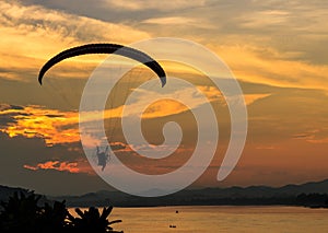 Silhouette flying paramotor over river and sunset sky