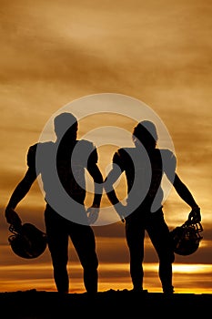 Silhouette of football players holding helmets in the sunset