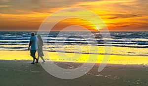 A silhouette of a foreign tourist couple happily walking together along a white sand beach