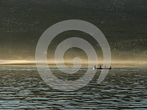 Silhouette of four men in canoe with paddles at forest background