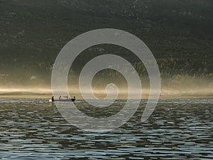 Silhouette of four men in canoe with paddles at forest background