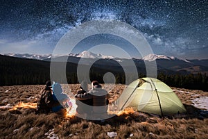 Silhouette of four people sitting together beside camp and tent under beautiful night sky full of stars and milky way