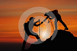 Silhouette of friend helping friend climbing up mountain by giving a hand