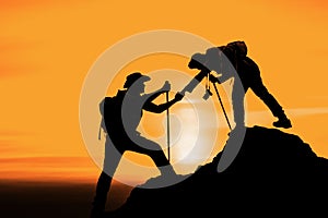 Silhouette of friend helping friend climbing up mountain by giving a hand
