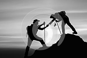 Silhouette of friend helping friend climbing up mountain by giving a hand