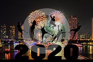 Silhouette of friends jumping celebrating new year over number 2020 on blurred city and river with fireworks background