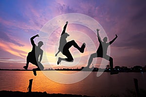 Silhouette of friends jumping over the lake on sunrise background, happy life, winning and achievement concept