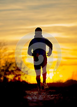 Silhouette front view of young sport man running outdoors in off road trail track with Autumn sun at orange sky sunset