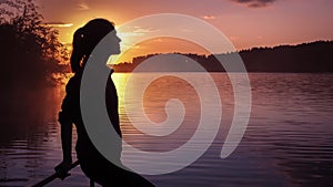 Silhouette girl background sun. Girl standing near water outdoors. Gold sunset lake. Young woman thinking about something river du