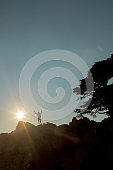 Silhouette of a girl with a backpack on a rock at sunset. The silhouette of the winner on the top of the mountain. The concept of