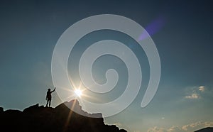 Silhouette of a girl with a backpack on a rock at sunset. The silhouette of the winner on the top of the mountain. The concept of