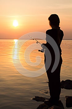 Silhouette of a girl on the bank of the river with a fishing rod