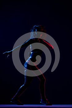 Silhouette of a girl dancing zumba. Side lit with blue and red lights on dark background