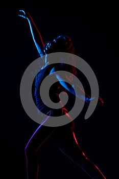 Silhouette of a girl dancing zumba. Side lit with blue and red lights on dark background