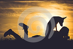 Silhouette of girl with dog relaxing by sunset.