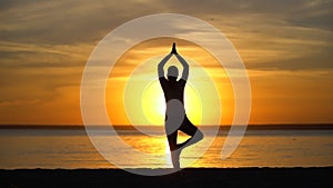 Silhouette girl doing tree yoga pose at sunset in nature outdoors. Sporty Yoga woman with open raised arms practicing