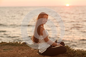 Silhouette of a girl doing yoga and mediation at sunset by the sea