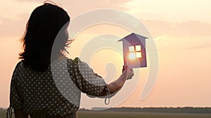 Silhouette of a girl in a dress holding a paper house against the sunset. Construction, real estate operations.