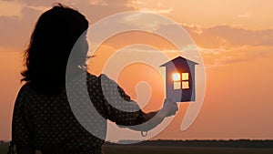 The silhouette of a girl in a dress holding a Paper house. Beautiful sunset at night. Family happiness and comfort.