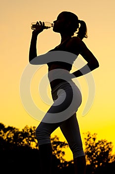 Silhouette of girl drinking water after outdoor workout