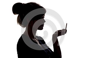 Silhouette of a girl with handpicked hair, profile of a woman face looking in a pocket mirror, the concept of the beauty and fashi
