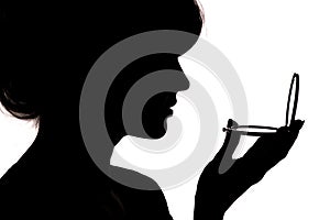 Silhouette of a girl with handpicked hair, profile of a woman face looking in a pocket mirror, the concept of the beauty and fashi