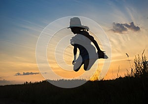 Silhouette of a girl in a hat, a little witch flies at dusk on Halloween against the backdrop of the sunset sky